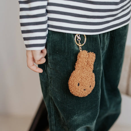 A child in a striped shirt and green corduroy pants adds an eco-friendly touch by showcasing a playful Miffy Keychain Terry Plush - Cream from their outfit.