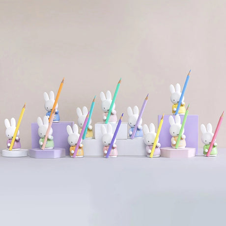 Twelve Miffy pen tray organisers in varied pastel outfits holding colored pencils arranged on white and lavender platforms