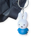 This charming Miffy Keychain - Classic by Miffy showcases a cartoon rabbit with white fur and black eyes, dressed in a timeless blue shirt. It comes with a stylish black strap, making it an ideal cute accessory for any collection.