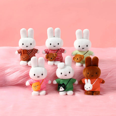 Six plush bunny toys wearing colorful outfits with small animal-shaped crossbody bags on soft pink surface