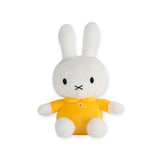 A gentle Miffy Plush Classic Yellow toy rabbit, featuring long ears and adorned in a yellow shirt, rests serenely against a plain white backdrop.