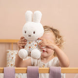 In a cozy crib adorned with pastel bedding, a child lovingly holds the Miffy Plush White & Vintage Flowers - 25cm, crafting a perfectly serene moment.