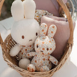 A Miffy Plush Vintage Flowers All Over toy cuddles with a white plush rabbit in a basket, accompanied by a folded pink blanket.