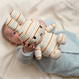 A baby lying down holds up a Miffy Plush Vintage Stripes All Over - 25cm toy, exuding timeless charm.