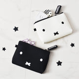 The Miffy Bunny Case White - 14cm from the Miffy brand features two silicone pouches, one in white and the other in black, both embellished with minimalist face designs and "miffy" tags that highlight Japanese design aesthetics. The light background is playfully decorated with scattered black star shapes, capturing the charm of the whimsical Miffy Bunny Case.