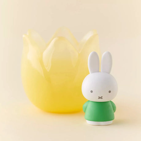 Miffy figure in green outfit standing next to translucent yellow tulip-shaped holder on beige background