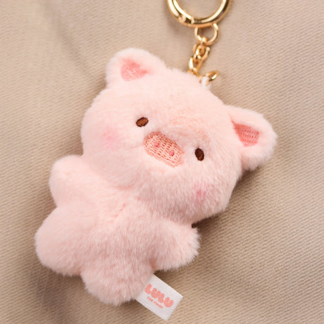 The LuLu The Piggy - Mini LuLu Keychain features a plush pink pig with a gold ring, shown on a beige fabric background.