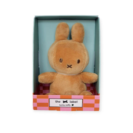 A soft chocolate beige Mini Miffy plush toy rabbit sits upright in a checkered pink and orange gift box labeled with "Miffy" and "Lucky Charm.