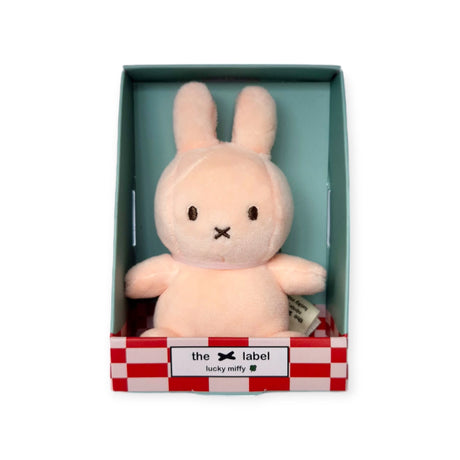 The Mini Miffy Plush in the Pink Lucky Charm edition, from the Miffy brand, features a neutral expression and comes in a teal and red checkered box labeled "the x label lucky miffy." This delightful charm makes for an ideal gift on any occasion.