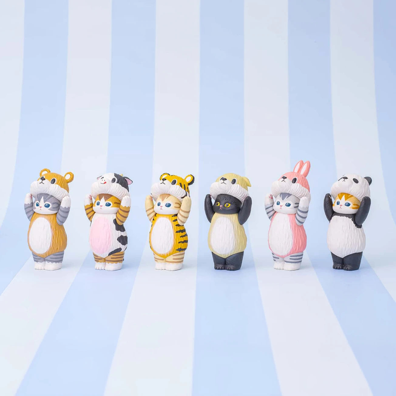 Six delightful animal-themed figurines from the Mofusand Premium - 8cm Adjustable Cat Blind Box collection stand with paws on their heads. These cats are adorned in different animal costumes against a light blue and white striped backdrop, adding a charming surprise element typical of the Blind Box series.