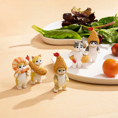 Five toy figures dressed in animal and vegetable-themed costumes stand on a table next to a plate with greens and tomatoes, reminiscent of a cat's favorite meal. These figures could be from the Mofusand Premium - Fried Shrimp Cat Blind Box collection by Mofusand.