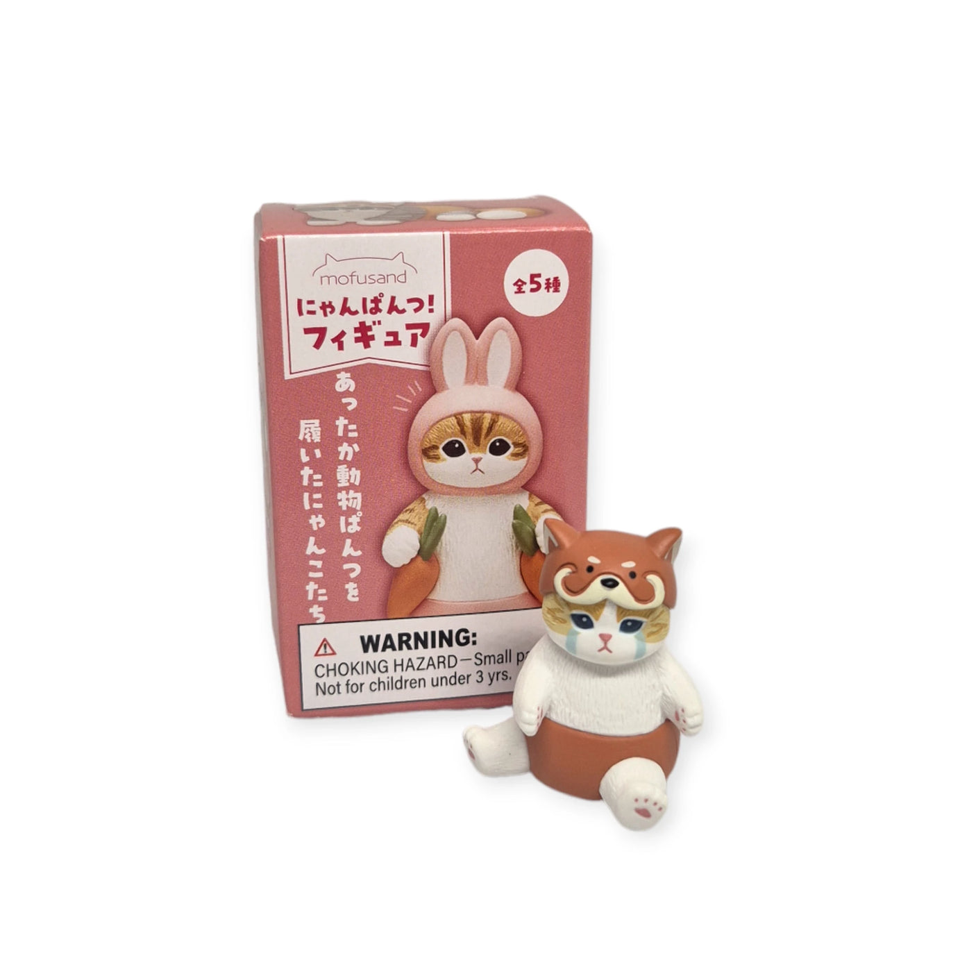 A small cat figurine dressed in a fox costume is positioned in front of a pink box featuring Japanese text, a warning label, and pictures of other Mofusand Premium - Nyanpantsu Blind Box collectibles from the series. Collect all to complete your charming set!