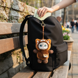 Plush red panda keychain hanging from black backpack with zip and strap