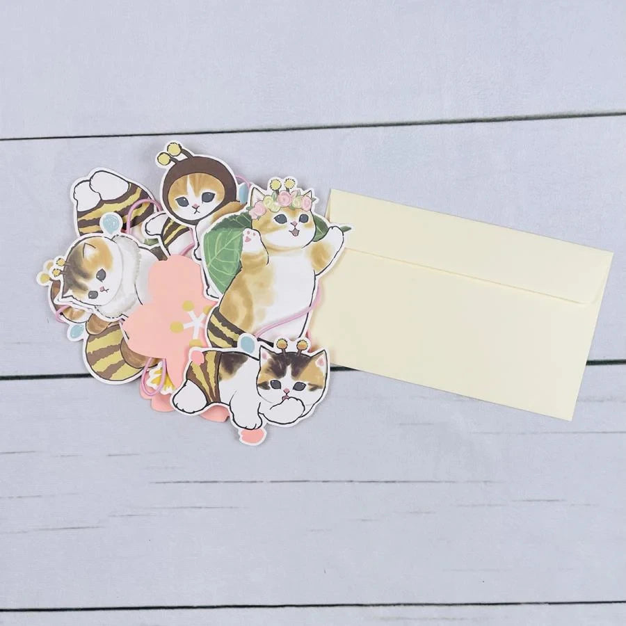 A set of charming Mofusand Spring Garland Decorations, showcasing Mofusand cats dressed as bees, is placed beside a cream-colored envelope on a light wood surface.