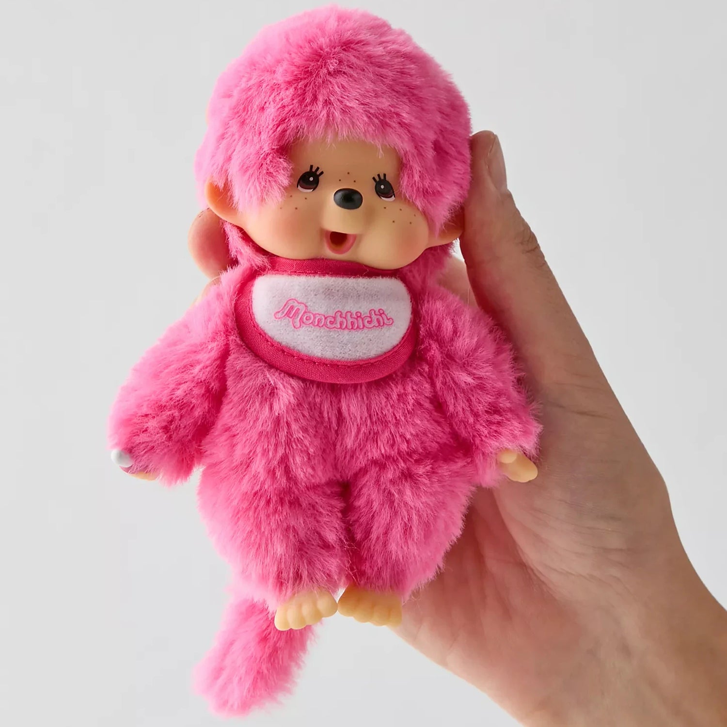 Monchhichi berry pink plush doll close-up, hood and logo scarf, held in hand