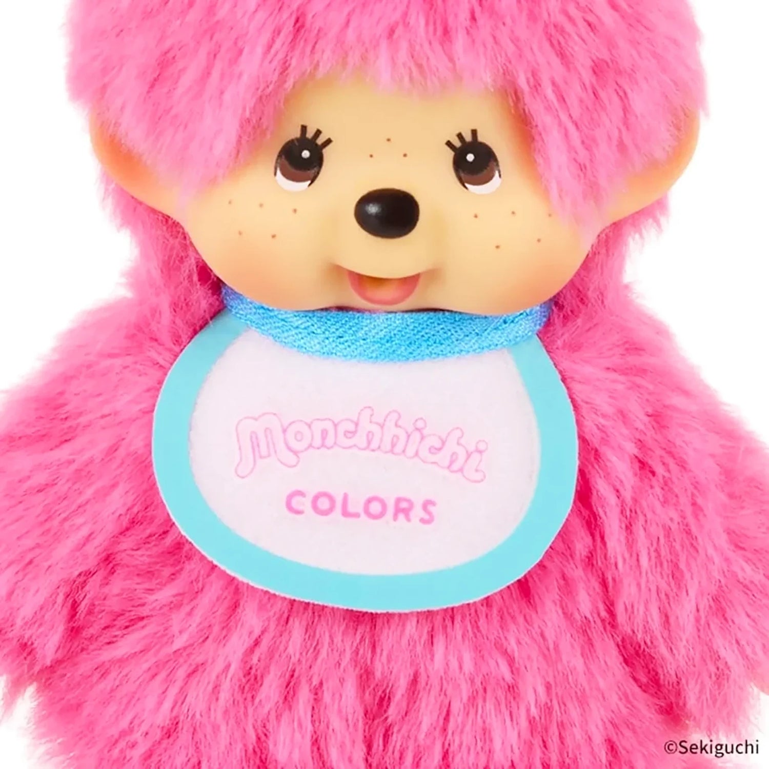 The Monchhichi Colours Bag Charm - Berry Pink by Monchhichi features a smiling plush doll with a blue and white "Monchhichi COLORS" bib—ideal as a cute bag charm or keychain gift.