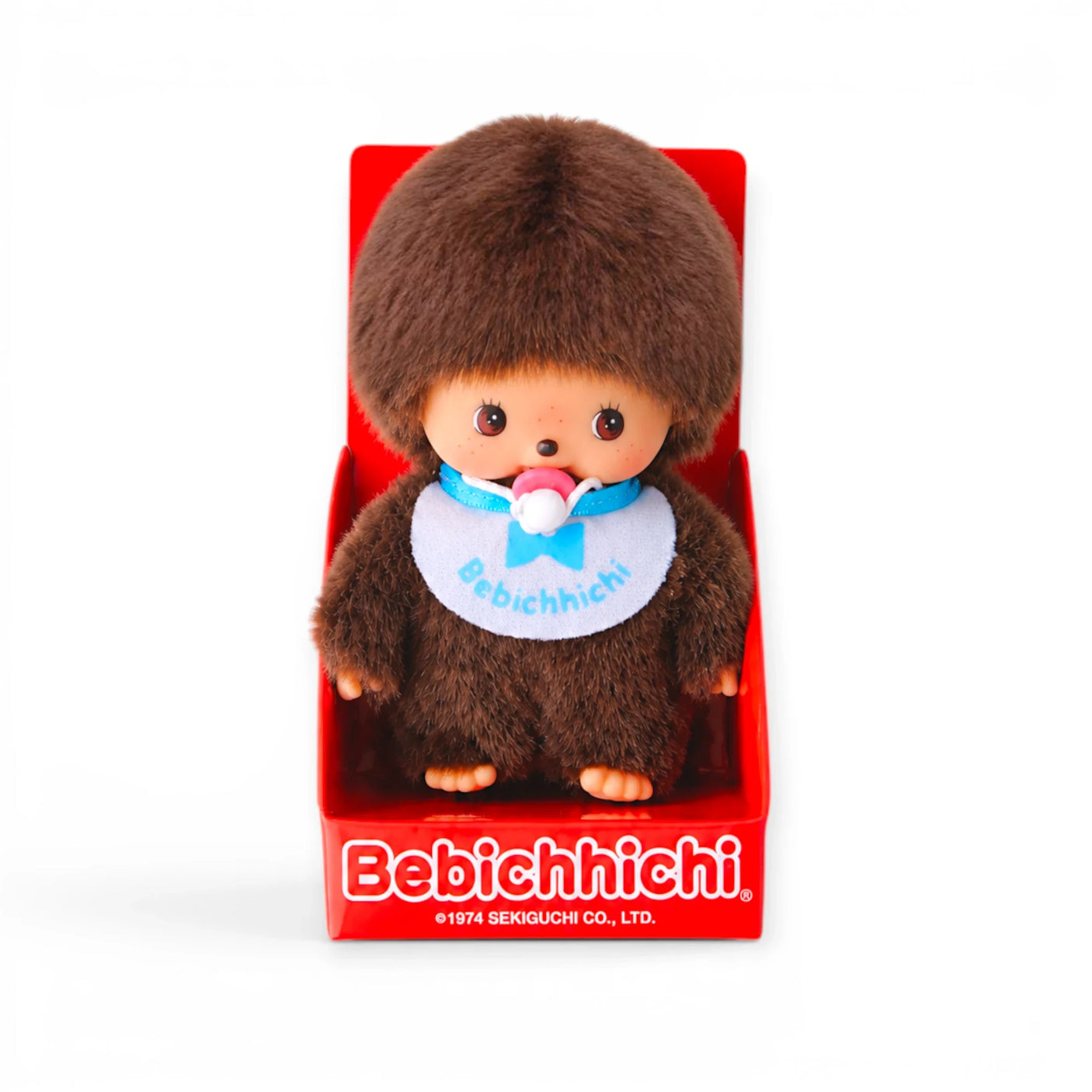Monchhichi plush doll with brown fur, blue bib and pacifier, in display box
