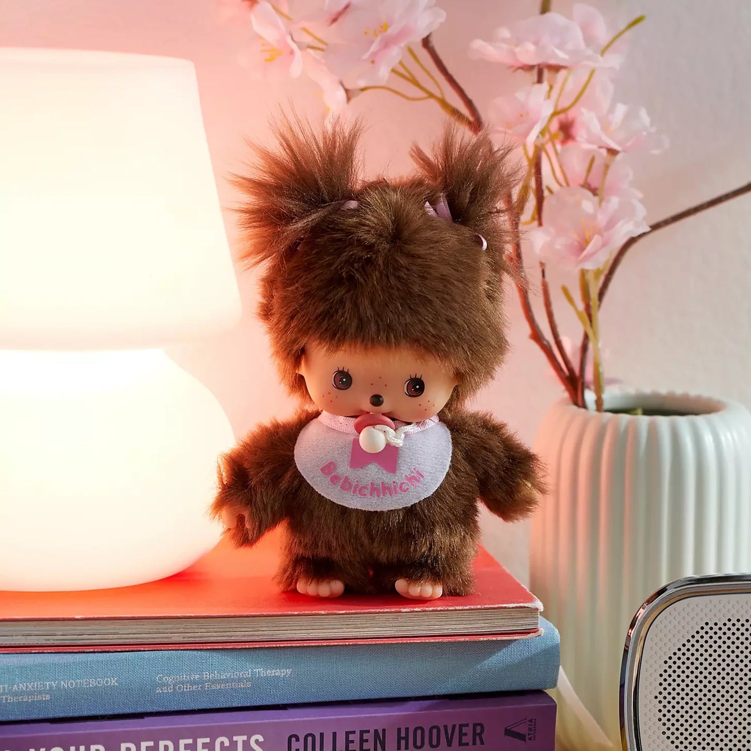 Brown plush doll standing upright, wearing a white bib with pink bow
