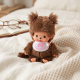 Brown plush baby doll with fluffy hood ears and white bib with pink bow