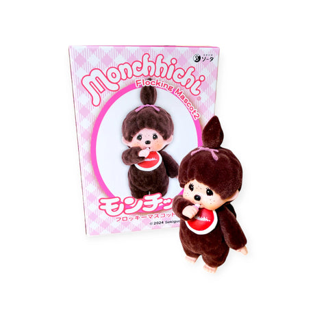 The Monchhichi Flocked Figure Blind Box - Original Series sits charmingly in front of its pink checkered box with Japanese text and logo. Its soft-touch finish enhances the delightful experience, reminiscent of a surprise find in a blind box.