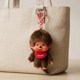 Brown plush boy bag charm hanging from red clip on beige tote bag