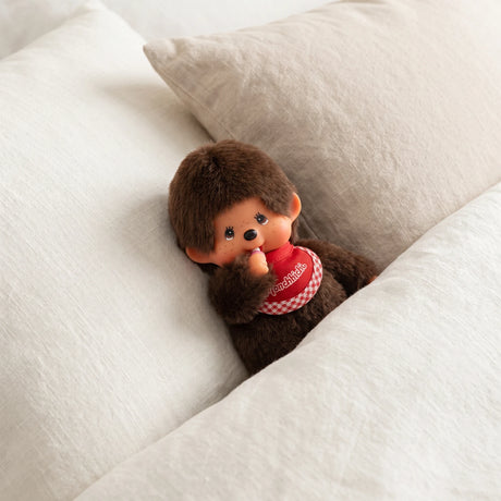 Monchhichi twin boy plush doll, dark brown fur, red plaid bib, on sofa cushion