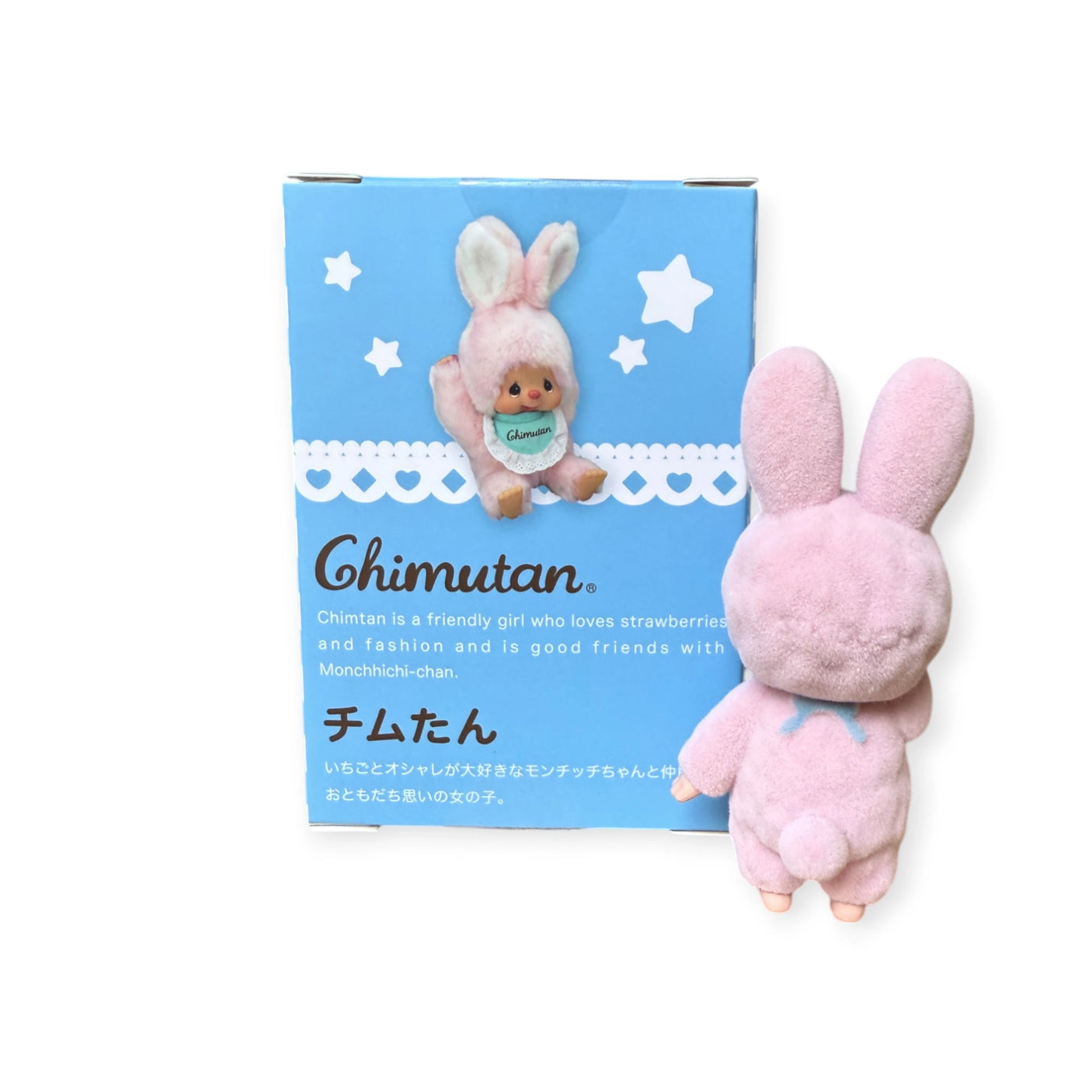 A pink plush bunny toy stands beside a blue box featuring the Monchhichi Flocked Figure Blind Box - Chimutan Series, with whimsical illustrations and text in the Monchhichi style.