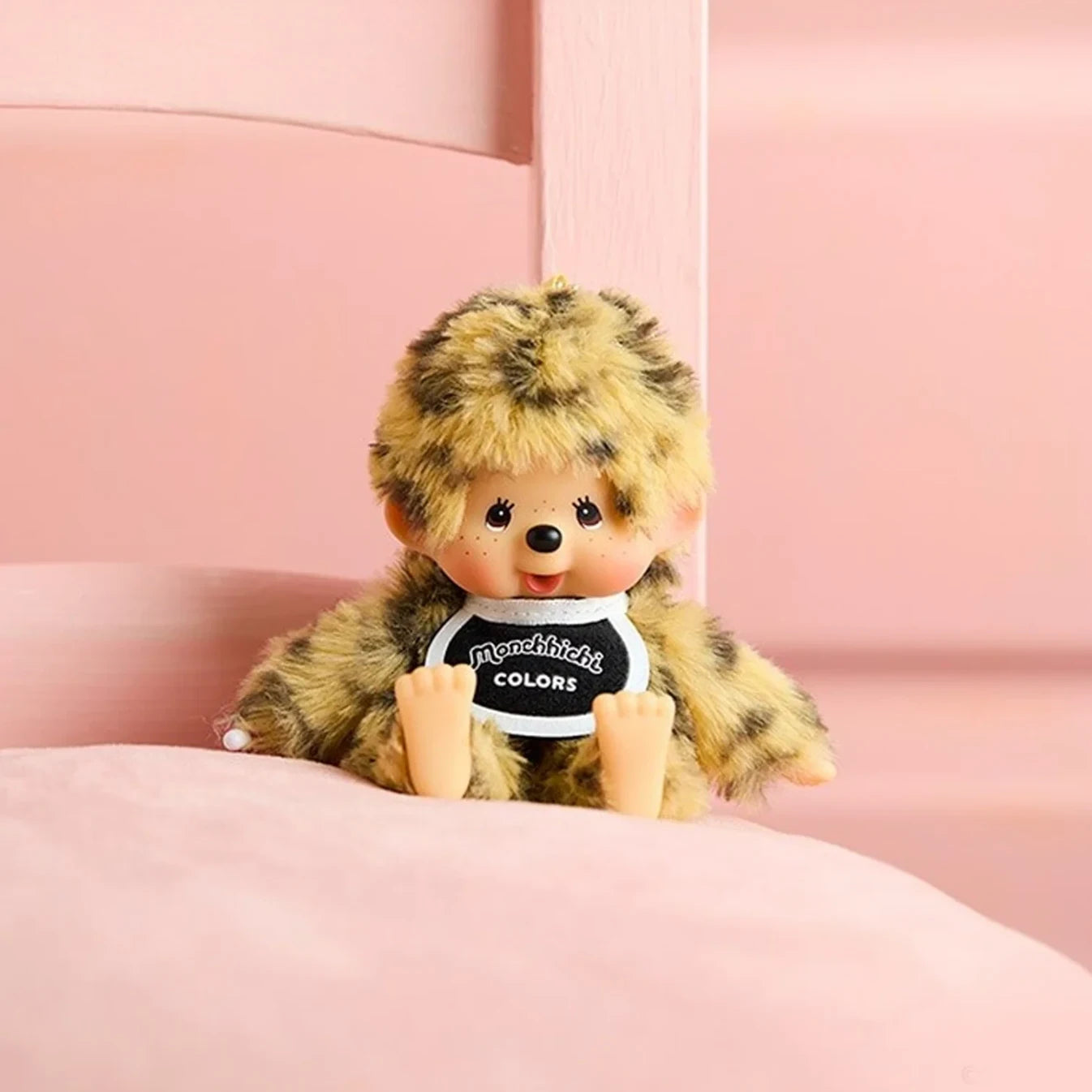 Leopard-pattern plush bag charm with round “Monchhichi COLORS” badge, seated