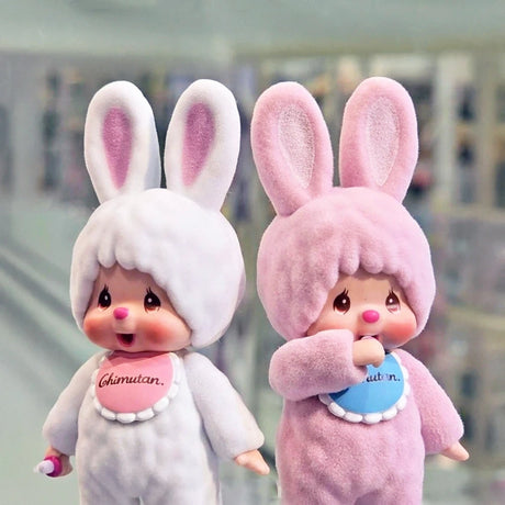 Two Monchhichi figures in rabbit costumes stand side by side. One is white with a "Chimutan" label; the other is pink. These charming Monchhichi Flocked Figure Blind Box - Chimutan Series dolls have large ears and blushing cheeks, capturing hearts with their delightful details.