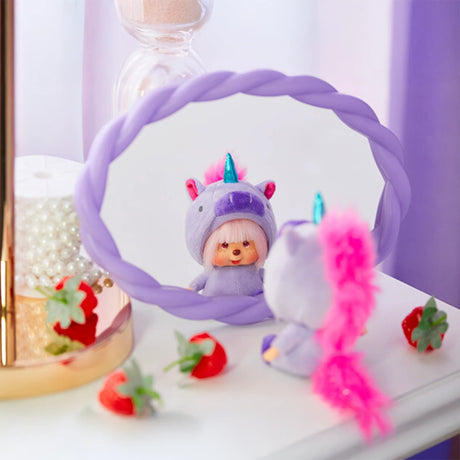 A limited-edition Monchhichi x 475 Harajuku Shinako Unicorn Keychain plush toy horse, dressed in purple with a pink mane, sits by a mirror. Its whimsical reflection is magical, while three scattered strawberries nearby finish the enchanting scene.