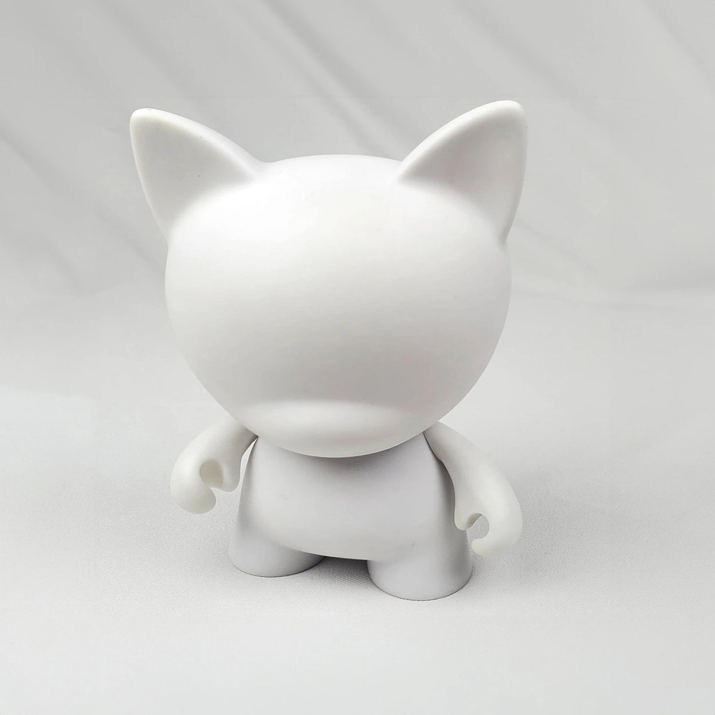 Introducing the Kidrobot Munnyworld - DIY Personalised Pop Vinyl mini figure, this plain white humanoid figurine with cat ears stands ready on a light surface, inviting creativity with its absence of facial features or distinct markings. Ideal for enthusiasts who enjoy crafting their own unique vinyl figures.