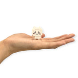 A hand holds a small, white block toy with a cartoonish face, including eyes, nose, and whiskers. This charming Nanoblock Chiikawa Figure Blind Bag brings whimsy to your collection with the excitement of discovering its delightful design inside.