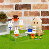 Animal-like toy figures, such as the Nanoblock Miffy Blind Bag - Vol. 3 figures, are showcased on transparent stands and a bench. A tiny house and basket are set in the background on a green surface, crafting a delightful scene reminiscent of a Blind Bag surprise by Nanoblock.