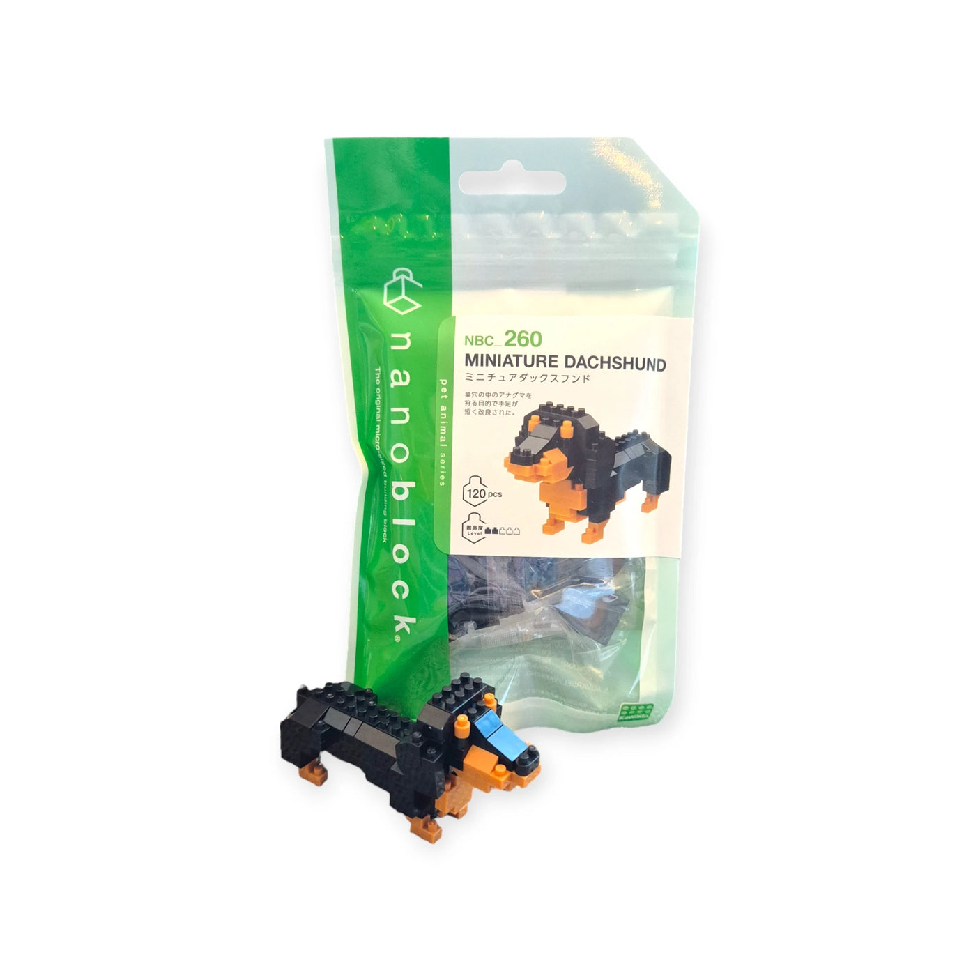 The Nanoblock Dachshund kit from Nanoblock includes a detailed miniature dachshund model prominently displayed in the foreground, highlighting its intricate micro construction, while the packaging in the background shows the product image and details.