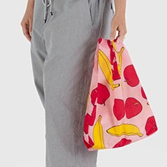 Person holding a pink tote bag with red and yellow fruit patterns, wearing gray pants.