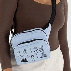 Person wearing a light blue crossbody bag with black illustrations, over a brown long-sleeve top and white pants.