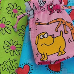 Colorful drawstring bags with cartoon animals and flowers on bright backgrounds; a green bag with flowers, a pink bag with a yellow dog, and a blue bag with red hearts.