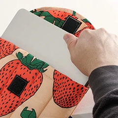 Hand placing a white tablet into a strawberry-patterned fabric sleeve.