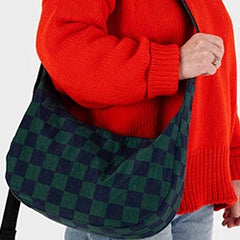 Person in a red sweater holding a dark green and black checkered shoulder bag.