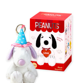 Plush Snoopy keychain wearing blue party hat with white stars next to red and white Peanuts-themed box