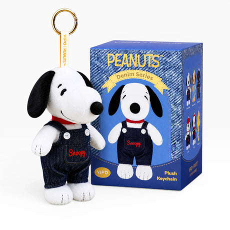 Snoopy plush keychain in dark denim overalls with hanging loop, beside Peanuts box