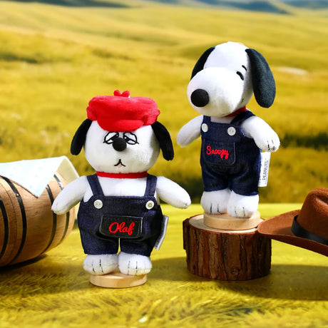 Two Snoopy-style plush keychains in dark denim overalls on wooden bases
