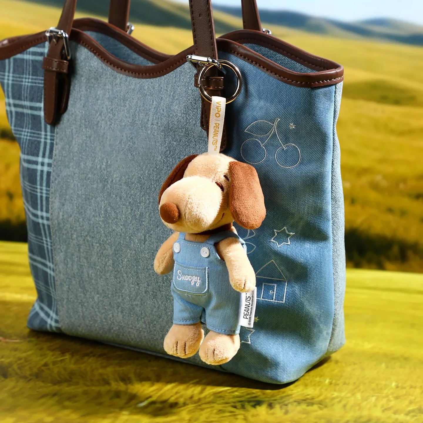 Denim tote bag with Snoopy plush keychain charm hanging on brown leather strap
