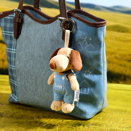 Denim tote bag with Snoopy plush keychain charm hanging on brown leather strap