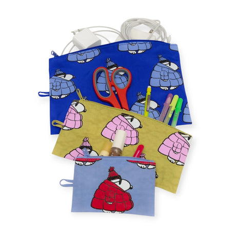 The Peanuts x Baggu Flat Pouch Set - Snoopy Puffer includes four zippered pouches made from recycled nylon featuring cartoon designs. They neatly hold a charger, scissors, colored pens, lipstick, and earbuds, with the Snoopy pouch adding a playful touch.