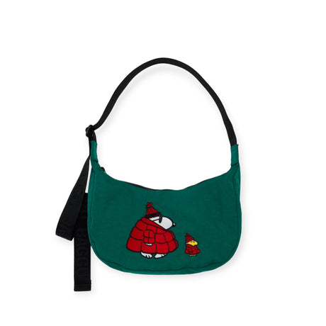 The Baggu x Peanuts - Medium Crescent Bag Embroidered Snoopy is a green shoulder bag crafted from recycled nylon with a black strap. It features an embroidered design of two cartoon figures in red winter clothing, facing each other. This stylish piece is perfect for fans of classic characters and is part of the Baggu x Peanuts collection.