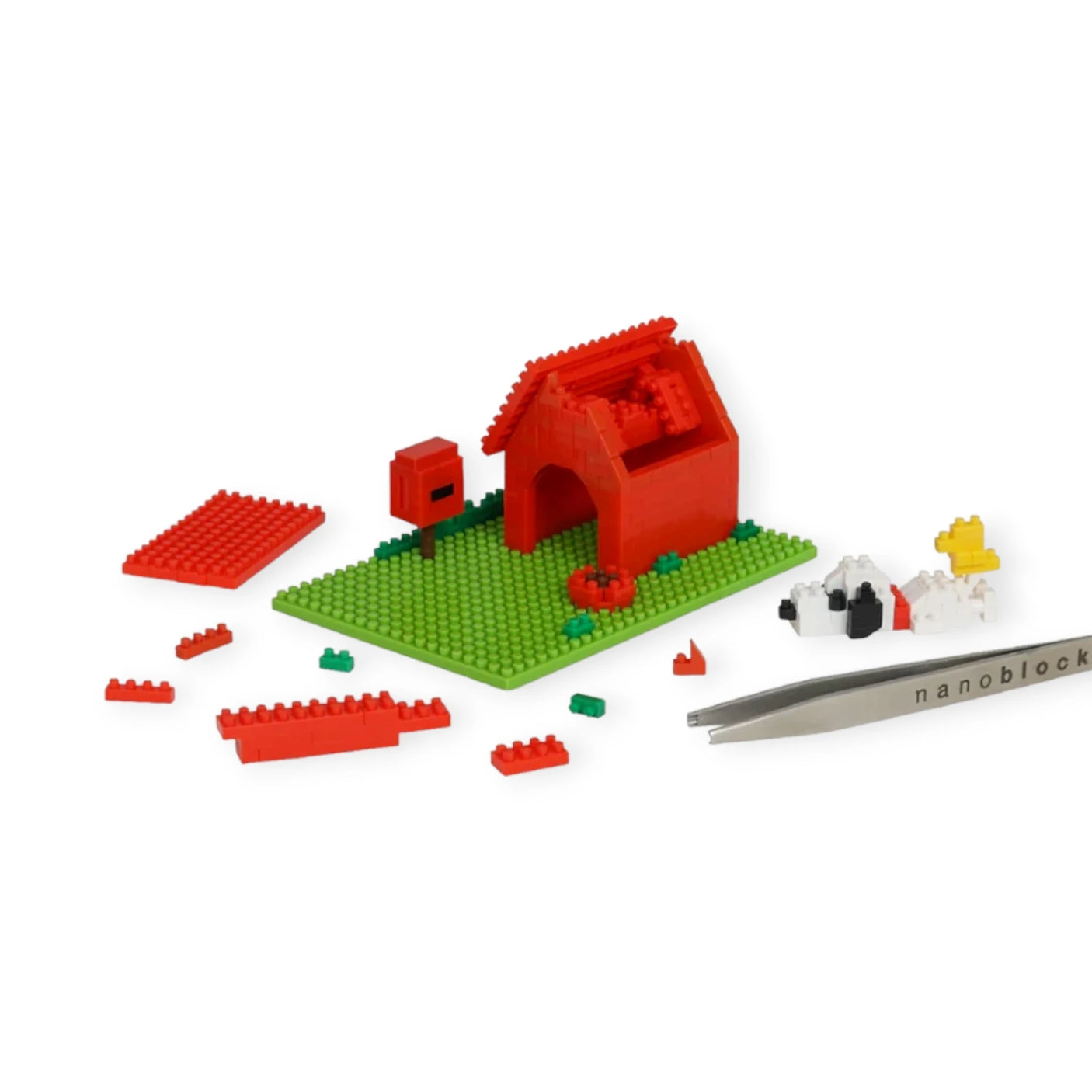 A partially constructed small red LEGO-like house sits on a green base, surrounded by scattered blocks, miniature animals, and tweezers labeled "nanoblock." The Nanoblock Peanuts - Snoopy House Set by Nanoblock beautifully encapsulates the charm of Peanuts history with its intricate detail using micro-sized blocks.