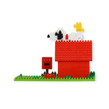 The Nanoblock Peanuts - Snoopy House Set, crafted by Nanoblock, features micro-sized blocks that come together to create a red doghouse with a figure resembling Snoopy perched on top and a little yellow bird resting on a green base, encapsulating the whimsical charm of Peanuts history.