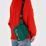 A person wearing a red sweater and jeans completes their outfit with an eco-conscious, durable green crossbody bag from Baggu, featuring adorable embroidery of the Peanuts Gang.