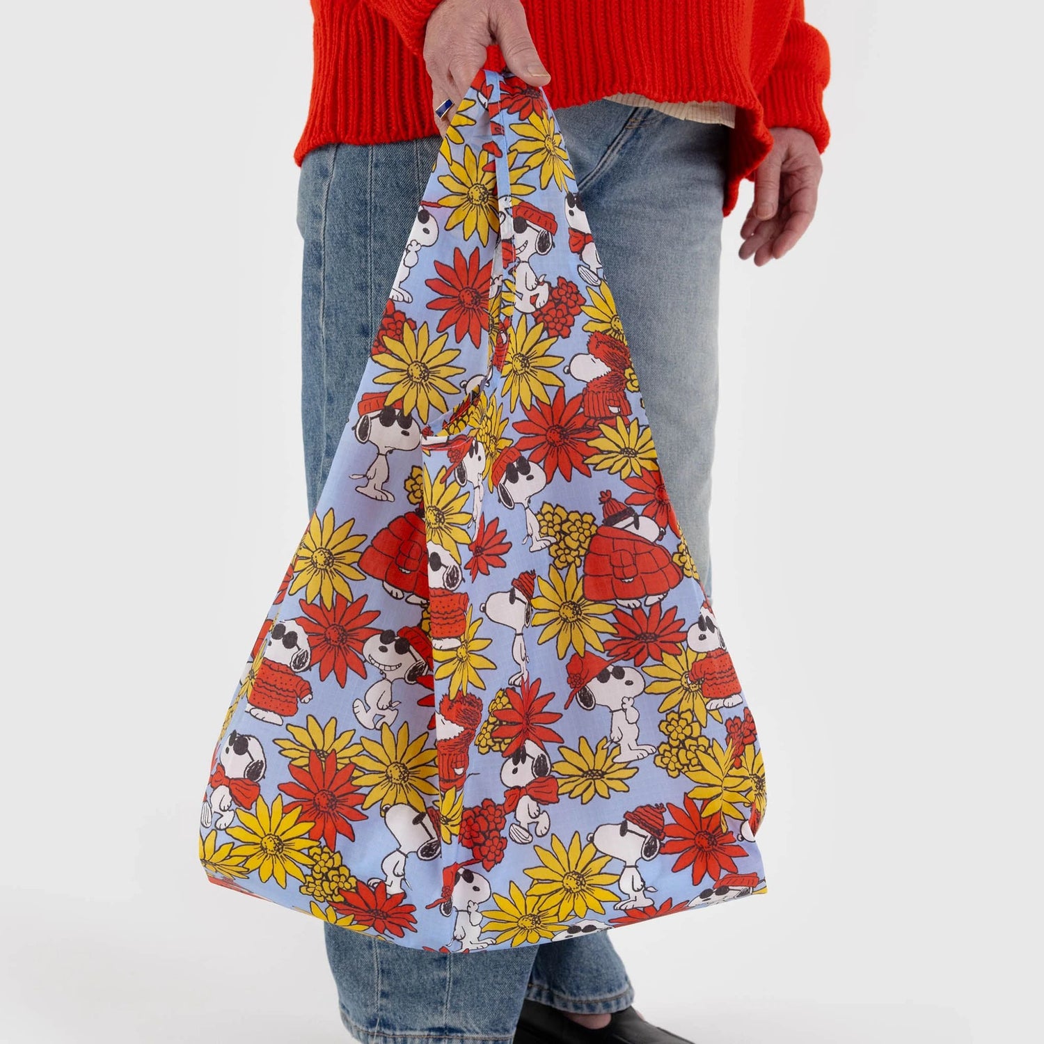 A person carries a Peanuts x Baggu Set of 3 Standard Bags - Floral Snoopy from Baggu, featuring cartoon animals, paired with a red sweater and jeans.